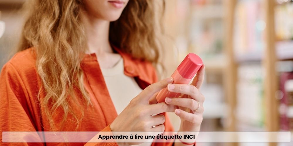 Femme en magasin cosmétique tenant un flacon rose et lisant attentivement l'étiquette INCI du produit